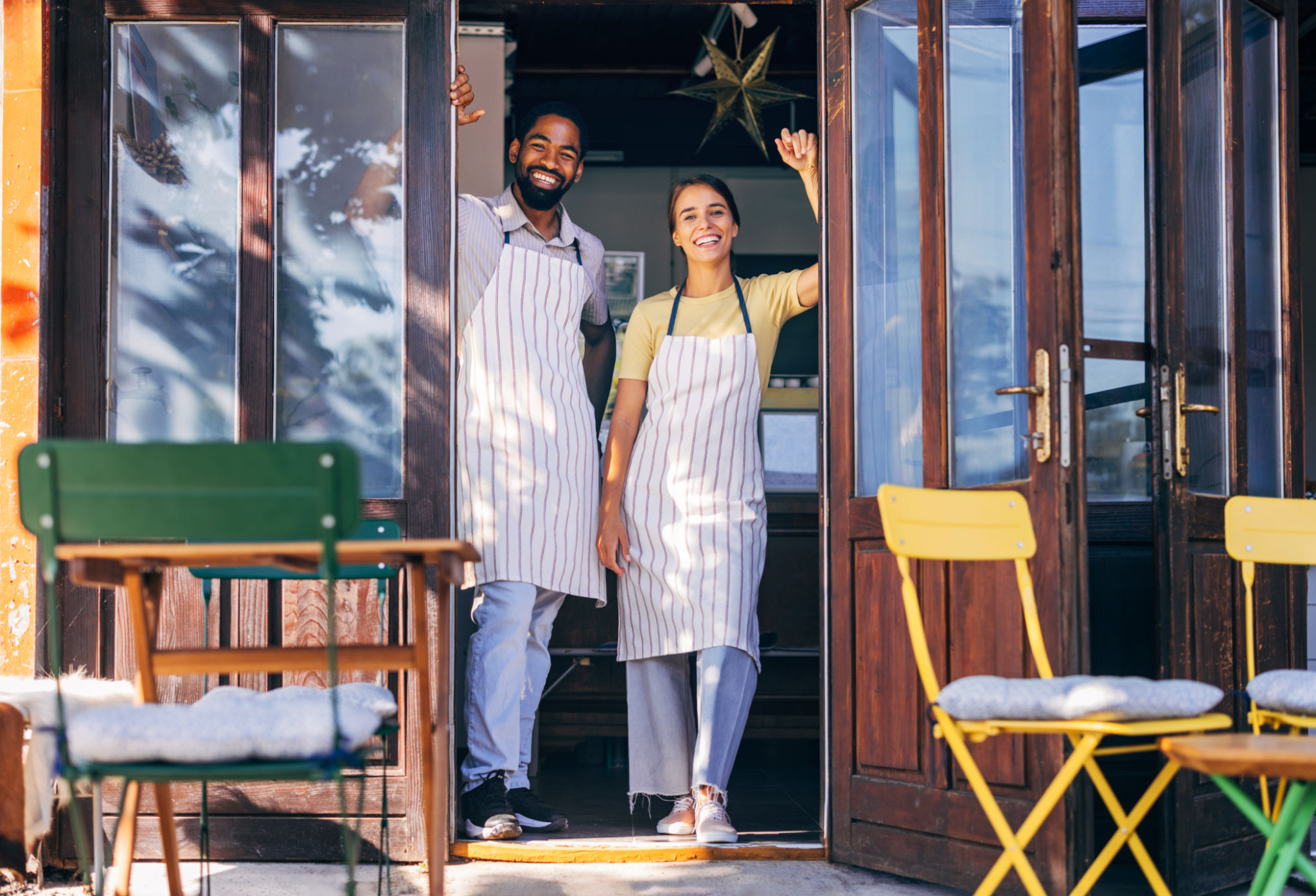 Smiling cafe owners welcoming customers at entrance
